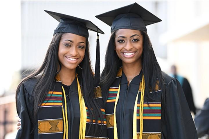 两个毕业生戴着帽子，穿着长袍，微笑着